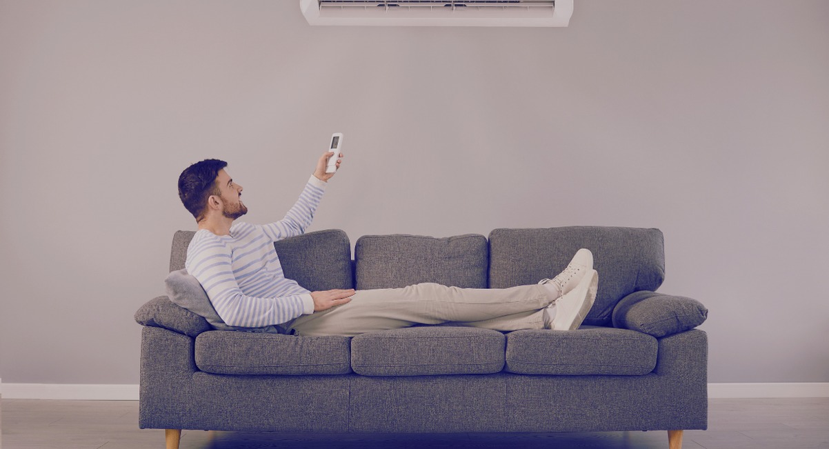 Homme allongé sur un canapé pointant la télécommande vers un climatiseur mural