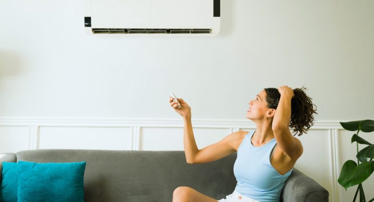 Femme sur un canapé actionnant la télécommande d'un climatiseur mural