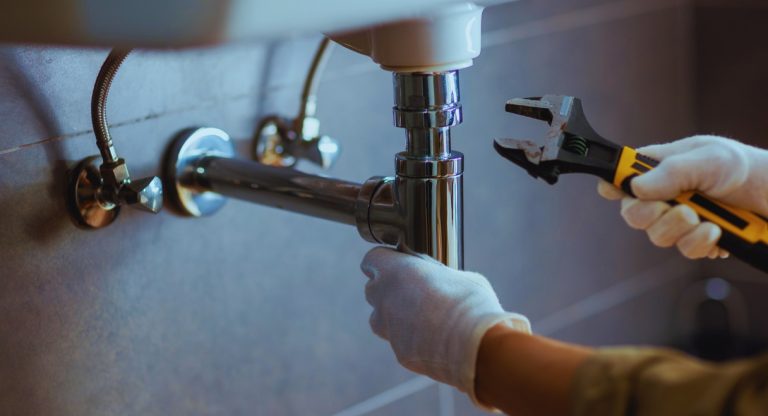 Technicien plombier réparant un siphon sous un évier avec une clé