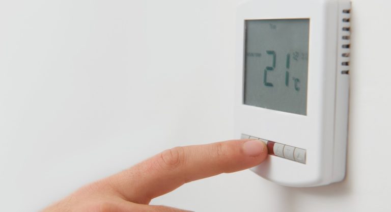 Main réglant la température sur un thermostat de chauffage mural